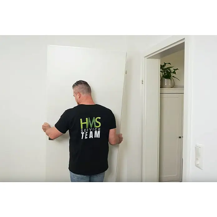 Türbandhaube TÜHZDE - Weiß, Aufbauhöhe 4 mm - Ein Mann montiert eine weiße Tür, wobei die Marke "HMS Service Team" auf seinem schwarzen T-Shirt zu sehen ist.