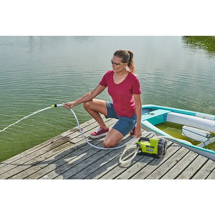 Ryobi ONE+ Akku-Gartenpumpe RY18TPXA - 18 V, Li-Ionen, Ohne Akku, Max. Fördermenge: 2.270 l/h - Eine Frau kniet neben einer Ryobi-Wasserpumpe am See und pumpt Wasser aus einem Boot, mit Schutzbrille und rotem T-Shirt.