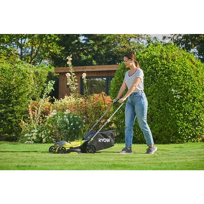 Ryobi ONE+HP Akku-Rasenmäher RY18LMX33A-0 - 18 V, Ohne Akku, Schnittbreite: 33 cm - Eine Frau, die einen RYOBI Rasenmäher im Garten benutzt, mit Bäumen und einem Gartenhaus im Hintergrund.