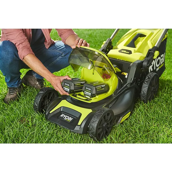 Ryobi Max Power Akku-Rasenmäher RY36LMX46A-150 - 36 V, 1 Akku, 5 Ah, Schnittbreite: 46 cm - Nahaufnahme eines Mannes, der zwei RYOBI-Akkus in einen RYOBI-Rasemäher einsetzt. Der Rasenmäher steht auf einer grünen Grasfläche.