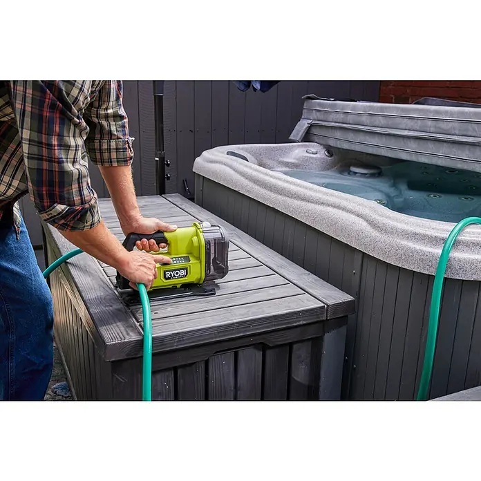Ryobi ONE+ Akku-Gartenpumpe RY18TPXA - 18 V, Li-Ionen, Ohne Akku, Max. Fördermenge: 2.270 l/h - Ein Mann bedient eine tragbare Ryobi-Pumpe auf einer grauen Holzkiste neben einem Whirlpool im Freien, mit einem grünen Schlauch angeschlossen.