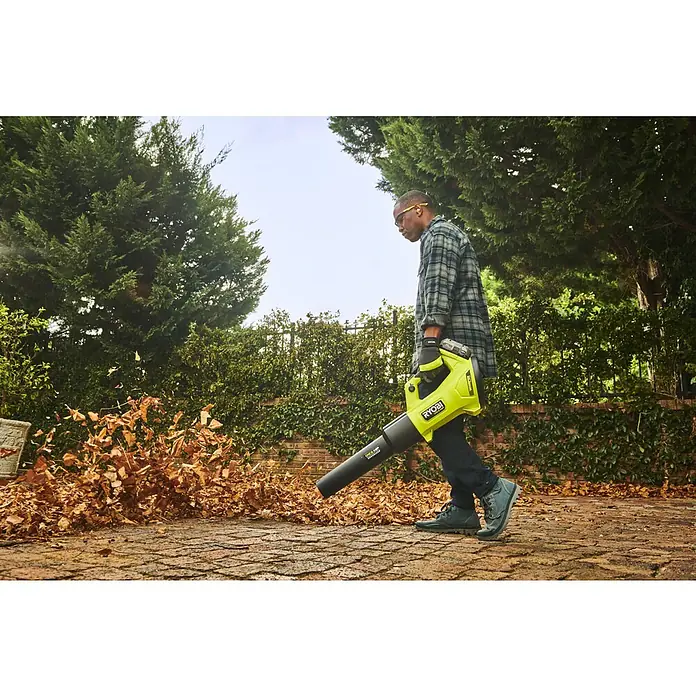 Ryobi ONE+HP Akku-Laubbläser RY18BLXD-0 Whisper - Ohne Akku, Blasgeschwindigkeit: 200 km/h, Blasleistung: 12,75 m³/min - Ein Mann benutzt einen hellgrünen Ryobi Laubbläser im Garten, um Laub zu entfernen, während er Schutzkleidung trägt.