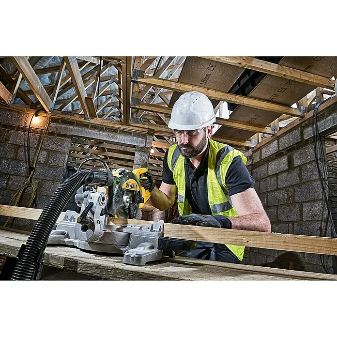 DeWalt Sierra ingletadora telescópica DWS774 - 1.400 W, 4.500 r.p.m., Diámetro hoja de sierra: 216 mm - Un trabajador de la construcción usa una sierra ingletadora DeWalt para cortar madera, con gafas de seguridad y casco. La sierra es el foco.