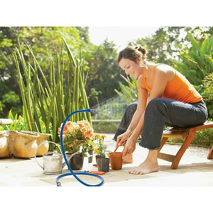 Orbit Nebulizador Cobra flexible - Apto para: Microriego - Mujer jardineando con una práctica manguera de riego azul con soporte, mientras está sentada en un banco de madera en el jardín.
