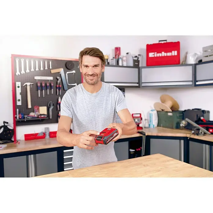 Einhell PXC 18V Batería - 18 V, 3 Ah - Hombre sosteniendo una batería Einhell Power X-Change en sus manos. La batería es roja y negra, mostrando la marca Einhell.