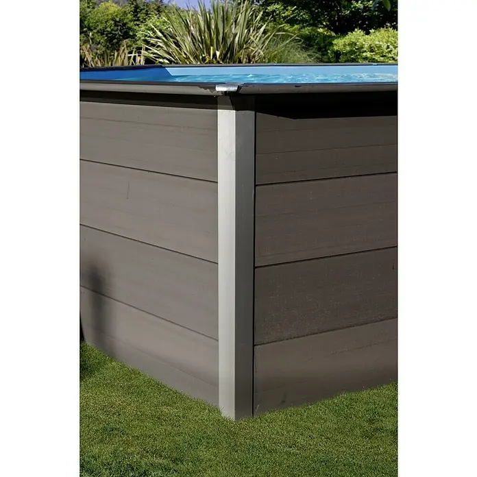 Gre Avantgarde WPC-Pool - L x B x H: 524 x 386 x 124 cm, 16.210 l, Dunkelgrau - Nahaufnahme der Außenseite eines grauen Whirlpools mit Holzstruktur und blauem Wasser, umgeben von grünem Gras und üppigem Grün.