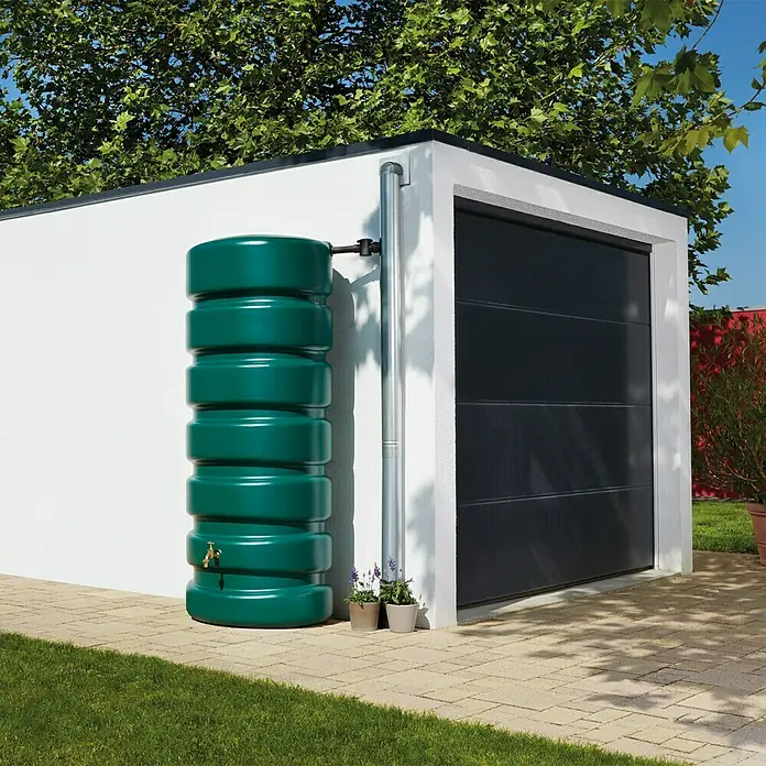 Garantia Basic Line Regentonne Classico - 2.600 l, Grün - Der grüne Regenwassertank steht neben einem Abflussrohr vor einer Garage. Perfekt zur Gartenbewässerung und Wasserspeicherung.