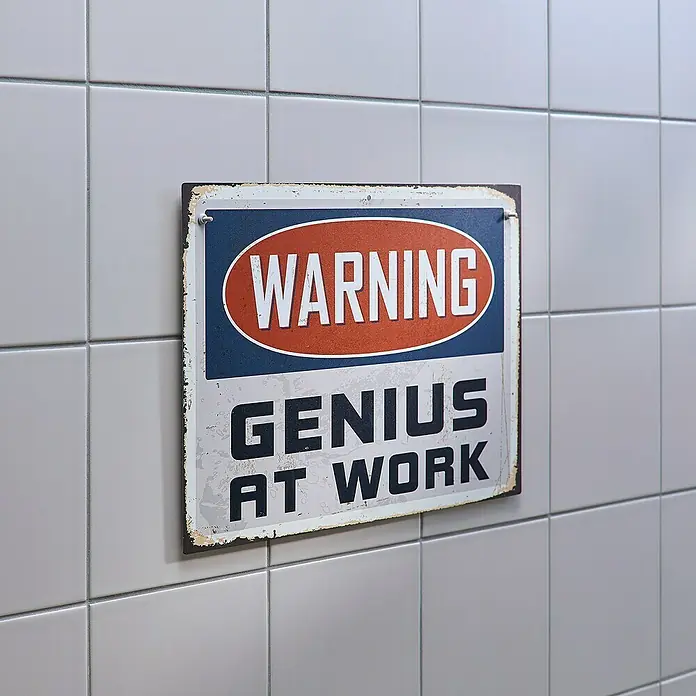 Tesa Verstellbare Klebeschraube - Geeignet für: Fliesen, Belastbarkeit: 3 kg, 2 Stk., Weiß - Ein Schild mit der Aufschrift "Warnung: Genie bei der Arbeit" hängt an einer gefliesten Wand. Das Schild ist im Vintage-Stil gehalten und hat abgenutzte Ränder.