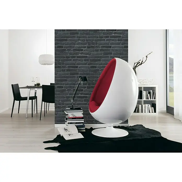 A.S. Création Vliestapete Cocktail 2 - Grau/Schwarz, Steinoptik, 10,05 x 0,53 m - Ein moderner Ei-Sessel in Weiß mit roter Innenausstattung steht auf einem schwarzen Teppich in einem stilvollen Raum.