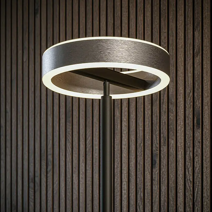 Tween Light LED-Stehleuchte Orlando - Höhe: 180 cm, Sandschwarz, Chrom, Warmweiß - Nahaufnahme einer stilvollen Stehlampe mit einem runden Lampenschirm und LED-Beleuchtung vor einer Holzwand.