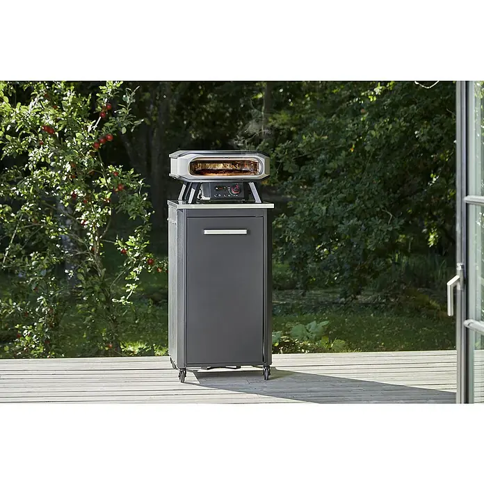 Cozze Pizzaofen Premium 17" - Grillfläche (B x T): 42,5 x 42,5 cm, 8 kW - Aufnahme eines Ooni Pizzaofens auf einem Unterschrank, der auf einer Holzterrasse im Freien steht.