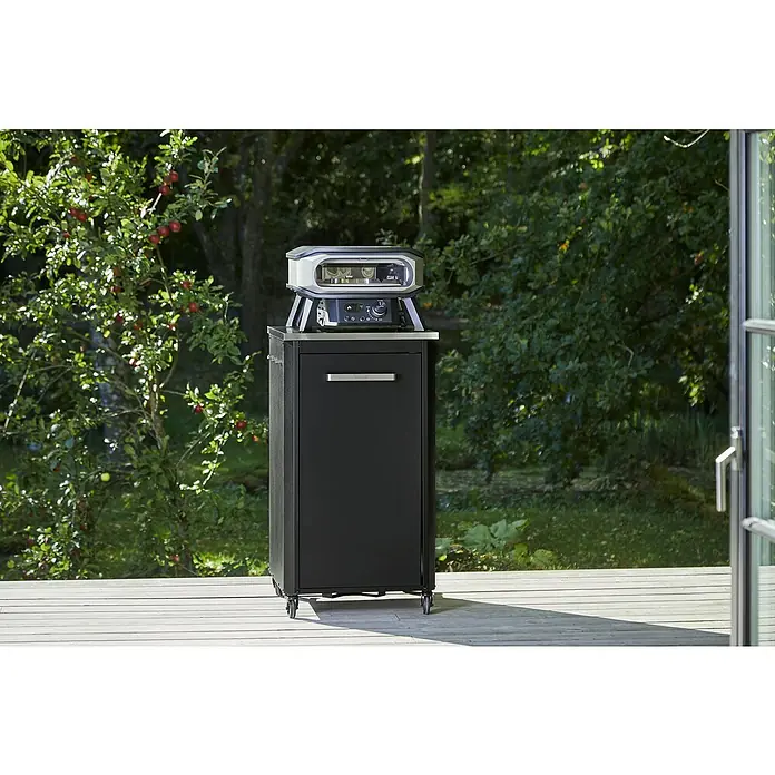 Cozze Pizzaofen Elektro Premium 13" - Grillfläche (B x T): 34 x 34 cm, 2,2 kW - Ein schwarzer Schrank mit einem Pizzaofen auf einer Holzterrasse vor einem üppigen Garten bietet kulinarische Möglichkeiten im Freien.