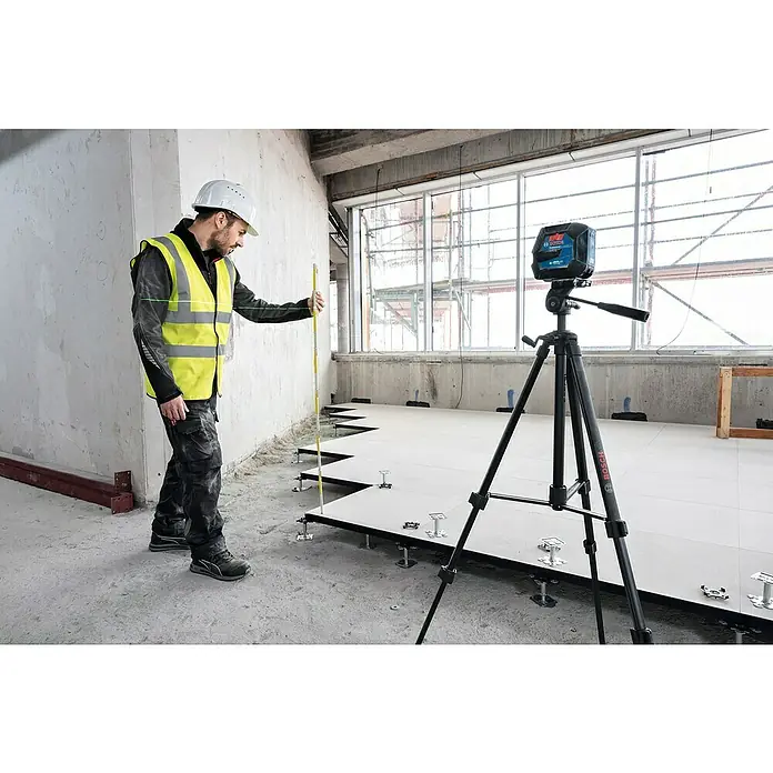 Bosch Professional Linienlaser GLL 20-22 G - Max. Arbeitsbereich: 20 m, Nivellierbereich: ± 0,3 mm/m, 5 -tlg. - Ein Bauarbeiter misst mit einem Bosch-Laser-Nivelliergerät, das auf einem Stativ steht, die Höhe in einem unfertigen Raum.