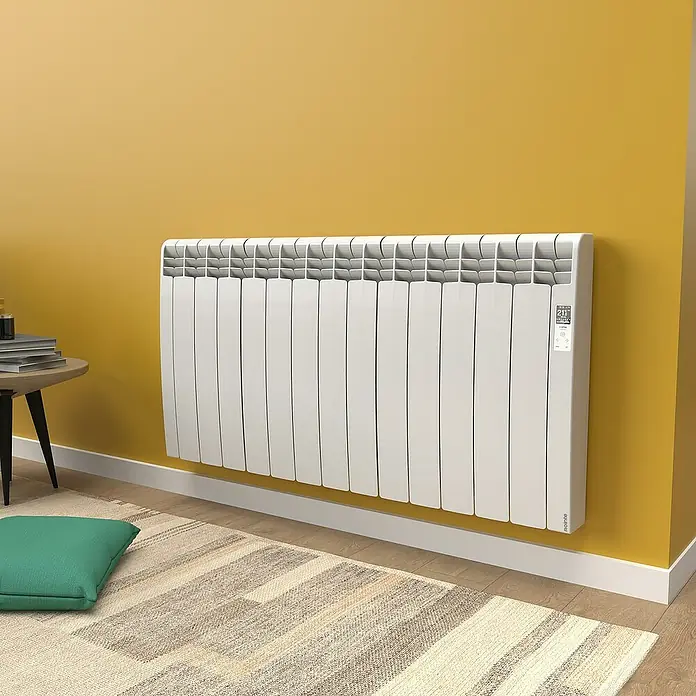 Rointe Emisor térmico Delta - 1.430 W, Blanco, 9,7 x 116 x 58,5 cm, Fluido - Primer plano de un radiador blanco de pared con pantalla digital sobre una pared color mostaza, que irradia calidez y confort.