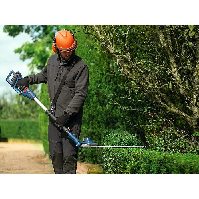 Bosch Professional AMPShare 18V Teleskop-Heckenschere GHE 18V-50 TP - 18 V, Ohne Akku, Schnittlänge: 50 cm - Ein Mann mit Helm und Gehörschutz trimmt mit einer Bosch Akku-Heckenschere eine Hecke. Das Gerät ist blau mit silberner Klinge.