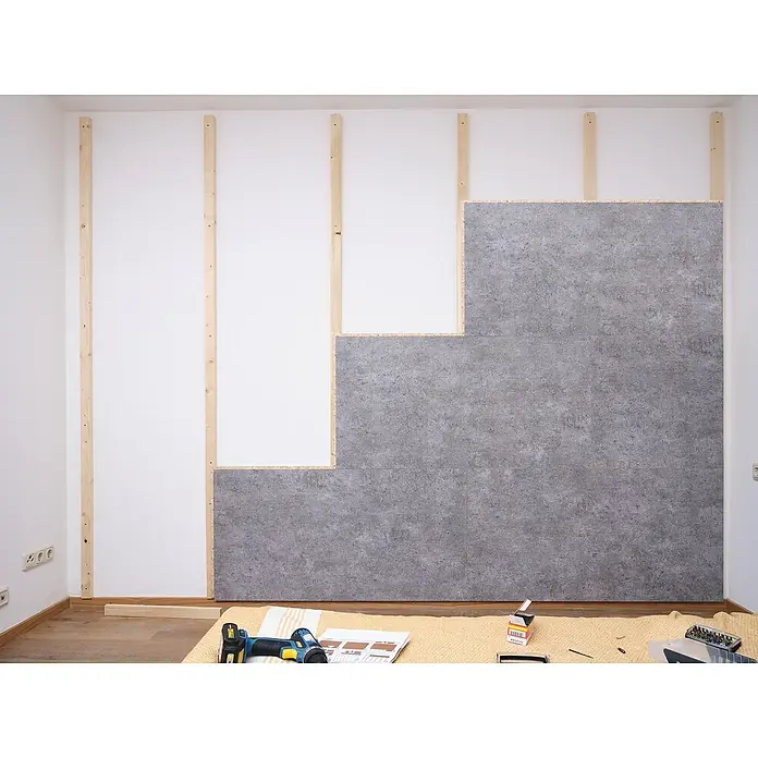 Egger Wandpaneel DecoWall - Rovigo Beton, 125 cm x 66 cm x 12 mm - Wandverkleidung aus grauen Betonplatten, die an Holzlatten an einer weißen Wand befestigt sind, teilweise montiert.