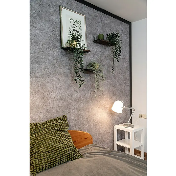 Egger Wandpaneel DecoWall - Rovigo Beton, 125 cm x 66 cm x 12 mm - Detailaufnahme eines Schlafzimmers mit rustikalen Wandregalen, Pflanzen und einer Nachttischlampe, die eine gemütliche Atmosphäre schaffen.
