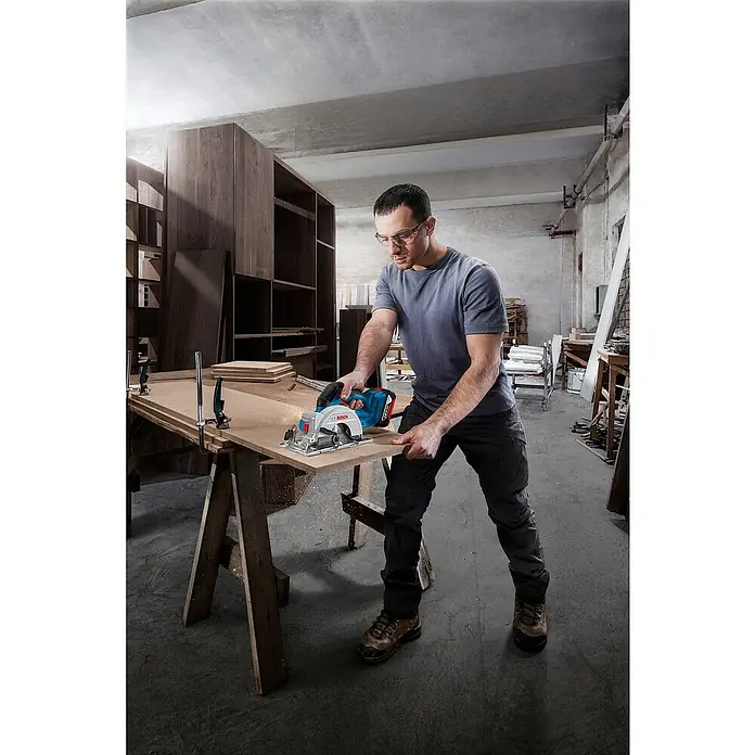 Bosch Professional AMPShare 18V Akku-Handkreissäge GKS 18V-51 - 18 V, Ohne Akku, 5.800 U/min - 6.300 U/min - Ein Mann arbeitet mit einer Bosch Akku-Handkreissäge an einem Holzbrett in einer Werkstatt. Die Säge ist blau und silbern.