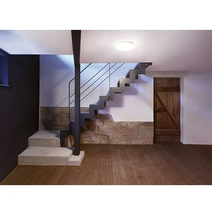 Steinel LED-Sensor-Deckenleuchte RS 16 LED S GLAS WW - 9,3 W, Weiß - Stilvolle Innenaufnahme eines Treppenhauses mit Akzentbeleuchtung und Holztür. Das Beleuchtungsdesign ergänzt die moderne Treppe perfekt.