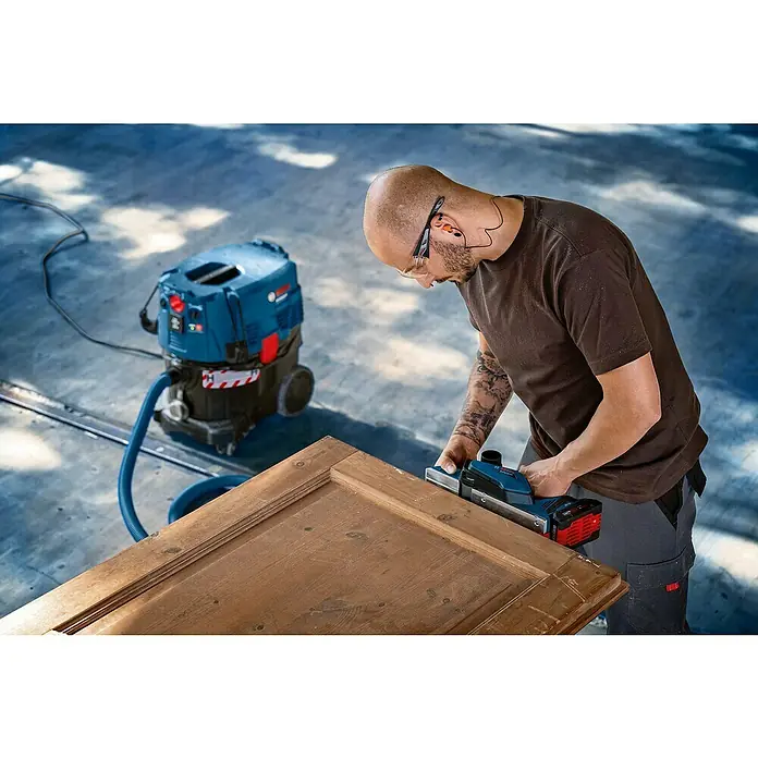 Bosch Professional AMPShare 18V Akku-Hobel GHO 18V-26 - 18 V, Ohne Akku - Ein Handwerker verwendet einen Bosch Hobel an einer Holztür, mit einem Staubsauger im Hintergrund.