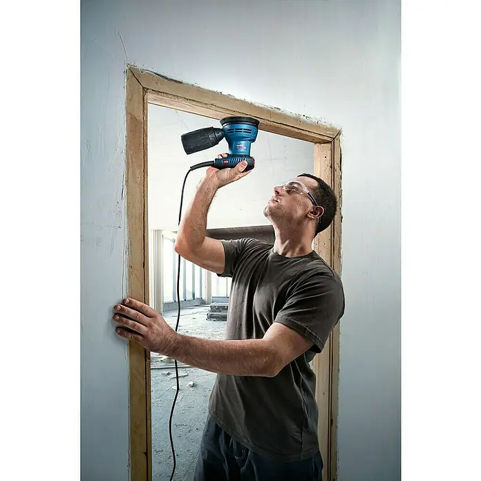 Bosch Professional Elektro-Exzenterschleifer GEX 125 - 290 W, Durchmesser Schleifteller: 125 mm - Ein Mann schleift einen Türrahmen mit einem blauen Bosch Exzenterschleifer, um die Oberfläche zu glätten.