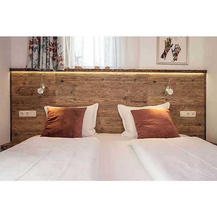 Egger Wandpaneel DecoWall - Namur Fichte Natur, 125 cm x 66 cm x 12 mm - Gemütliches Schlafzimmer mit Doppelbett, rustikaler Holzvertäfelung, Nachttischlampen und dekorativen Kissen für eine entspannte Atmosphäre.