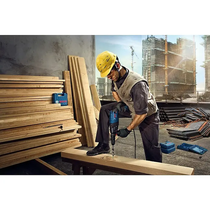 Bosch Professional Kombihammer GBH 240 - 790 W, 2,7 J, SDS-Plus-Aufnahme - Ein Bauarbeiter bohrt mit einer Bosch-Bohrmaschine ein Loch in ein Holzbrett vor einer Baustellenkulisse.
