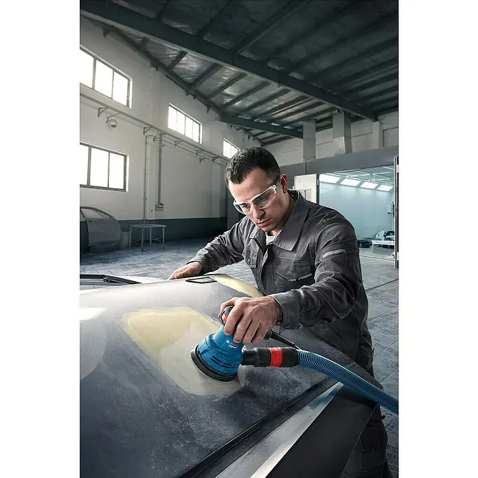 Bosch Professional Elektro-Exzenterschleifer GEX 125 - 290 W, Durchmesser Schleifteller: 125 mm - Ein Handwerker verwendet einen Exzenterschleifer, um die Oberfläche eines Autoteils zu bearbeiten. Das Werkzeug ist blau und hat einen Schlauch für Staubabsaugung.