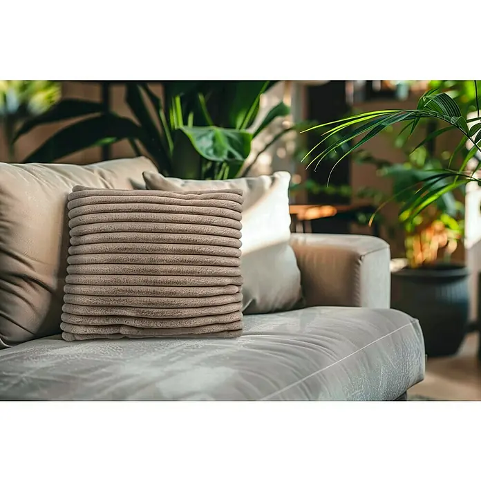 Kissen Plush - Taupe, 45 x 45 cm, 100 % Polyester - Nahaufnahme eines gerippten, quadratischen Kissens auf einem bequemen Sofa mit Pflanzen im Hintergrund, das ein gemütliches Ambiente schafft.