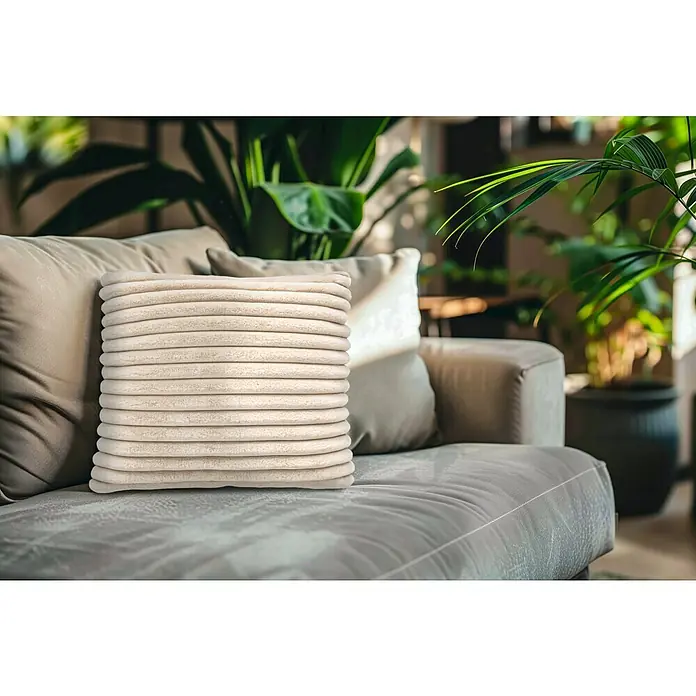 Kissen Plush - Beige, 45 x 45 cm, 100 % Polyester - Nahaufnahme eines gerippten Kissens auf einem Sofa, das Textur und Komfort betont und eine gemütliche Atmosphäre schafft.