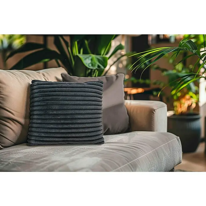 Kissen Plush - Graphite, 45 x 45 cm, 100 % Polyester - Nahaufnahme eines stilvollen grauen Kissen mit Rippenmuster auf einem beigen Sofa, das eine gemütliche und moderne Wohnatmosphäre schafft.