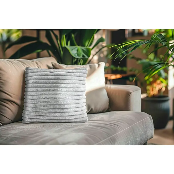 Kissen Plush - Silber, 45 x 45 cm, 100 % Polyester - Nahaufnahme eines gerippten, rechteckigen Kissens auf einer Couch mit anderen Kissen und Pflanzen im Hintergrund, das eine gemütliche Atmosphäre schafft.