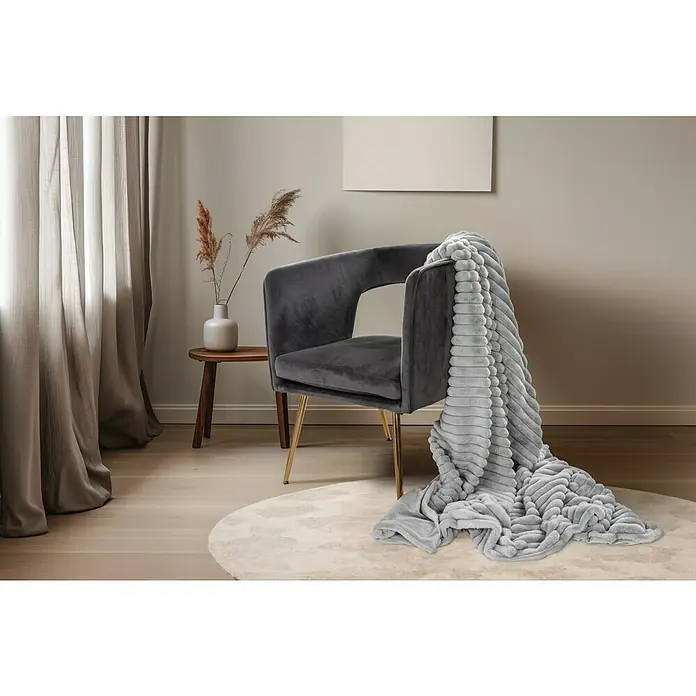Decke Plush - Silber, 200 x 150 cm, 100 % Polyester - Ein grauer Sessel mit goldfarbenen Beinen und eine weiche, graue Decke darauf, die auf einem runden Teppich drapiert ist.