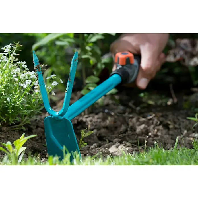 Gardena Combisystem Kleinhacke - Arbeitsbreite: 5 cm, Blattform: Gerade, Anzahl Zinken: 2 - Nahaufnahme einer türkisfarbenen Gartenhacke mit zwei Zinken und einem Spatenblatt, die in einem Garten verwendet wird.