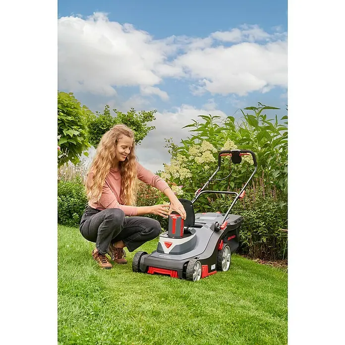 AL-KO Comfort Akku-Rasenmäher 38.5 Li - 36 V, 1 Akku, 4 Ah, Schnittbreite: 38 cm - Eine Frau setzt einen Akku in einen AL-KO Rasenmäher auf einer grünen Rasenfläche ein. Der Akku-Rasenmäher ist grau mit roten Akzenten.