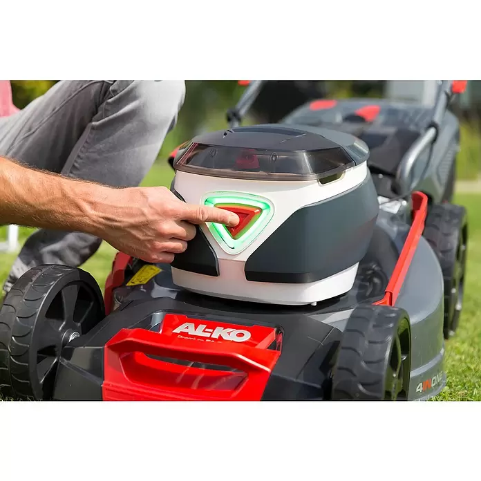 AL-KO Premium Akku-Rasenmäher 512 Li VS-W - 36 V, 2 Akkus, 4 Ah, Schnittbreite: 51 cm - Hand drückt den beleuchteten roten Einschaltknopf eines grau-roten AL-KO Rasenmähers.