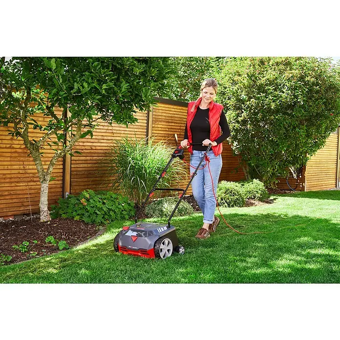 AL-KO Elektro-Vertikutierer 32.4 Basic Care - 1.200 W, Arbeitsbreite: 32 cm - Frau arbeitet im Garten mit einem Rasenlüfter mit roten Akzenten. Das Gerät ist ein praktischer Helfer für die Gartenpflege.
