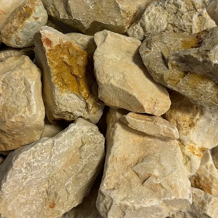 Hamann Mercatus Bruchsteine Kalkstein - Sandbeige, Körnung: 30 mm - 60 mm, 25 kg - Ein Haufen heller, unregelmäßig geformter Steine mit bräunlich-orangen Mineraleinschlüssen.