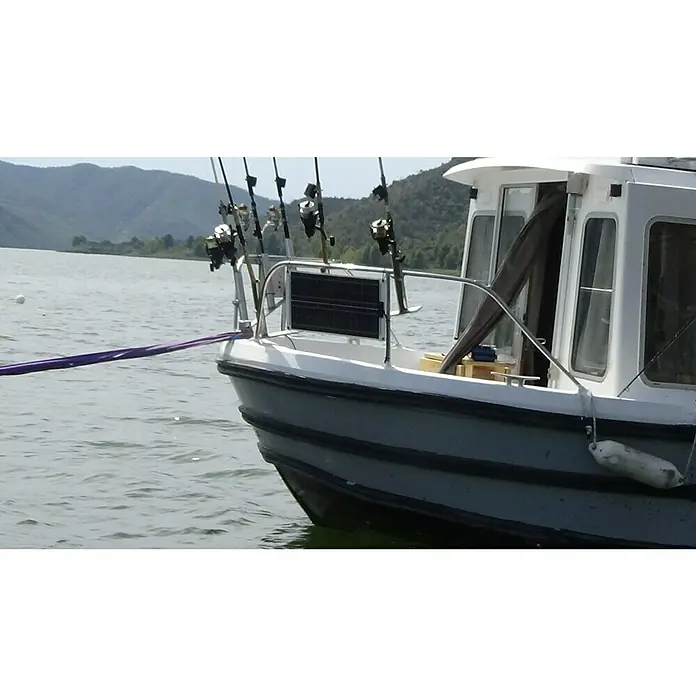 Sunset Solarmodul-Set Laminat - Nennleistung: 30 W, Für Booten, Yachten und Wohnmobilen - Nahaufnahme eines Fischerbootes mit Angelruten, das auf einem ruhigen Gewässer vor einer Bergkulisse ankert.