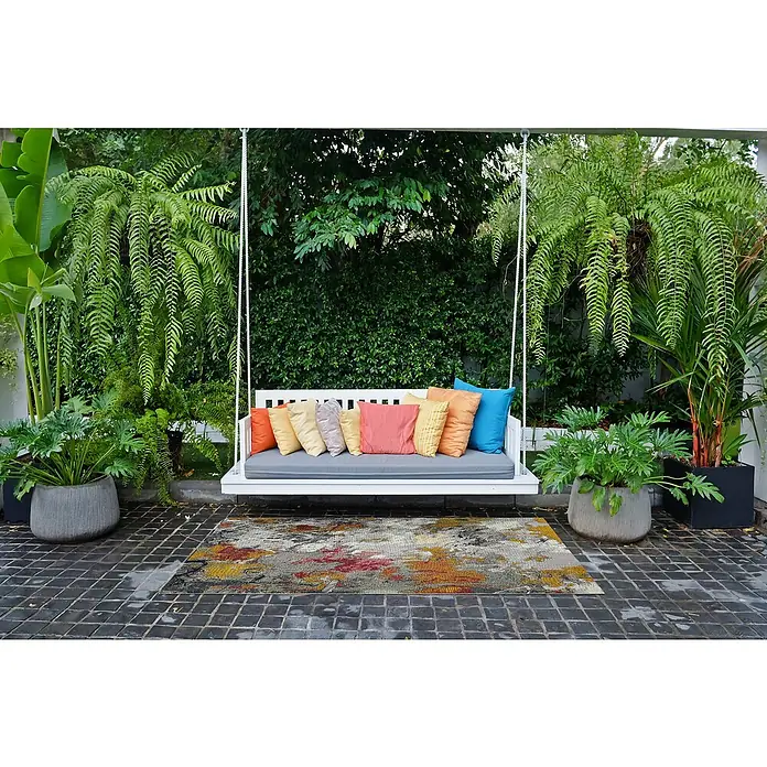 Outdoor-Teppich Portland - Grau/Bunt, 235 x 160 cm, 75 % Polypropylen, 25 % Polyester - Einladende Gartenszene mit einer Schaukelbank, bunten Kissen und üppigem Grün, die zum Entspannen im Freien einlädt.