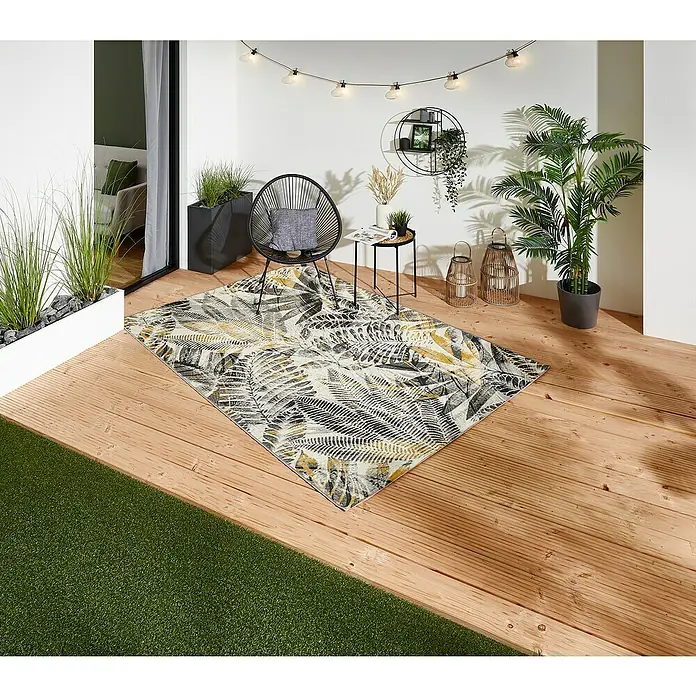 Outdoor-Teppich Portland - Grau/Gelb, 235 x 160 cm, 75 % Polypropylen, 25 % Polyester - Ein rechteckiger Teppich mit Blattmuster in Schwarz, Gelb und Weiß liegt auf einer Holzterrasse im Freien und sorgt für einen stilvollen Akzent.