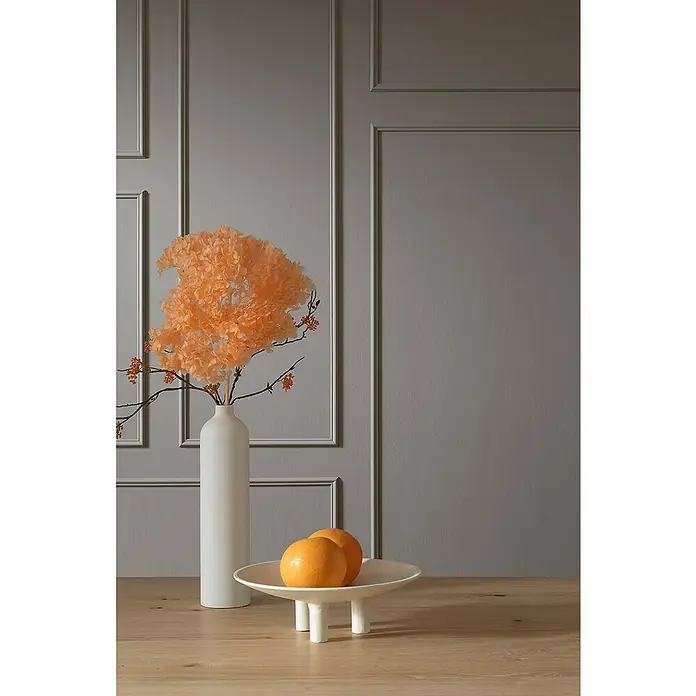 SCHÖNER WOHNEN-Kollektion Zierprofil Wandleiste Elegant 4 - 200 cm x 11 mm x 22 mm, Hochverdichtetes extrudiertes Polymer (HDPS) - Stillleben mit schlanker Vase, floralem Arrangement, Obstschale mit Orangen auf hellem Holztisch vor grauem Hintergrund mit Wandpaneelen.