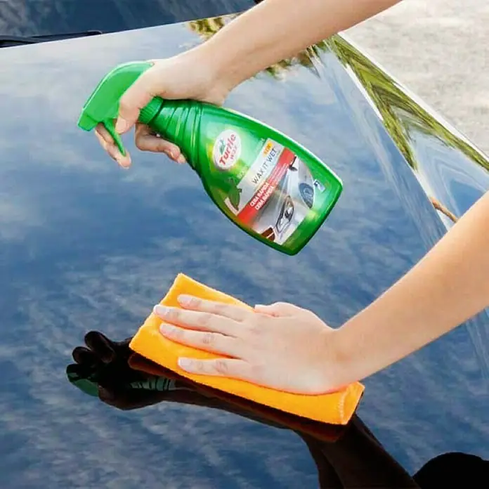 Turtle Wax Limpiador abrillantador de cera rápida - 500 ml - Una persona que aplica Turtle Wax It Wet a un coche. La cera está en un frasco rociador verde y el coche es negro.