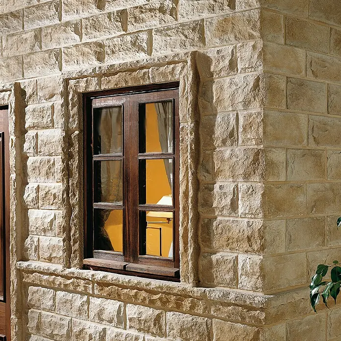 Moldura decorativa angular Petra Arena - 30 x 30 x 11 cm - Primer plano de una ventana con marco de madera en una fachada de mampostería de piedra natural, creando un ambiente rústico y cálido.