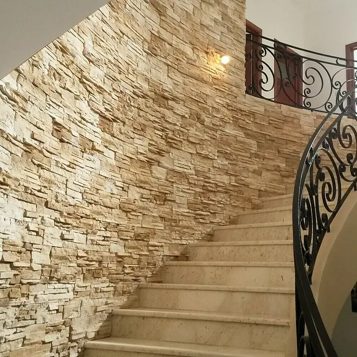 Revestimiento de piedra Petra Arena - Cantidad total: 4 pzs., Arena - Elegante escalera con pared de piedra decorativa que crea un ambiente cálido y acogedor. La barandilla negra complementa el diseño.