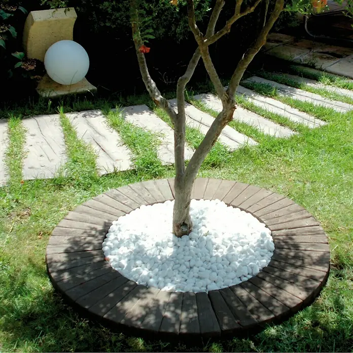 Paso para árboles Nogal - Marrón - Un árbol con un lecho circular de piedra y guijarros blancos, enclavado en la hierba verde, proporciona una estética de jardín cuidada.