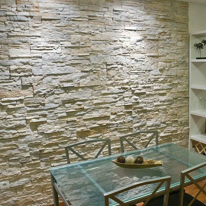 Revestimiento de piedra Petra Cuarzo - Cantidad total: 4 pzs., Cuarzo - Una toma detallada muestra una pared de piedra moderna combinada con una mesa de comedor de vidrio y metal, suavemente iluminada.