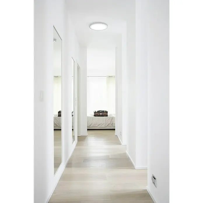 Ledvance LED-Deckenleuchte rund Silara - 16 W, Ø x H: 300 x 85 mm, Silber, Weiß, Neutralweiß - Einbauleuchte in einem modernen, minimalistischen Flur, der ein sauberes, helles Ambiente mit glatten, weißen Wänden und einem Holzfußboden betont.