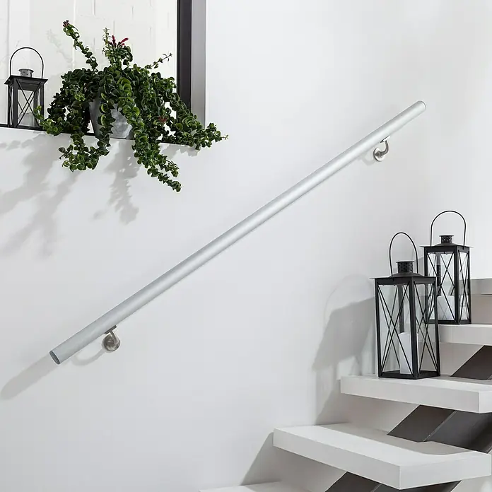 Treba Frewa Handlauf-Set H20 - Aluminium, Silber, Länge: 1.500 mm - Treppengeländer aus Aluminium an einer weißen Wand mit dekorativen Laternen auf den Stufen und einer Pflanze an der Wand.