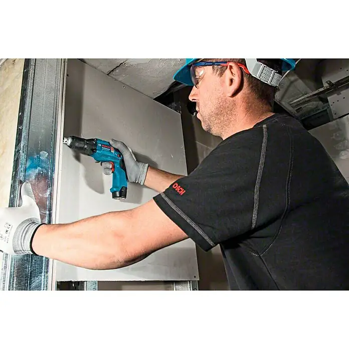 Bosch Professional Atornillador para placas de yeso de batería GTB 12V-11 - 12 V, 2 baterías, 2 Ah - Un trabajador de la construcción utiliza un taladro inalámbrico Bosch para fijar paneles de yeso a una estructura metálica.
